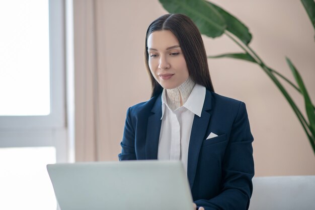 Von zuhause aus arbeiten. Hübsche junge dunkelhaarige Frau, die an einem Laptop arbeitet