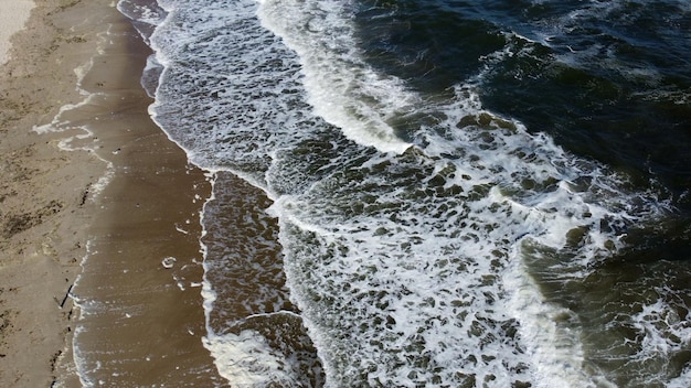 Vôo aéreo de drone sobre belas ondas do mar na praia de areia com espuma branca