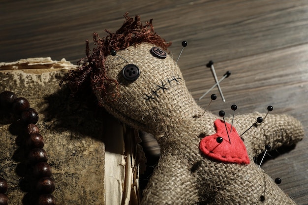 Voodoo-Puppe mit Pins altes Buch und Perlen auf Holztisch Nahaufnahme