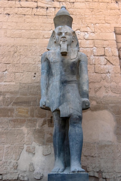 Vor einer Steinmauer steht eine Statue eines ägyptischen Pharaos.