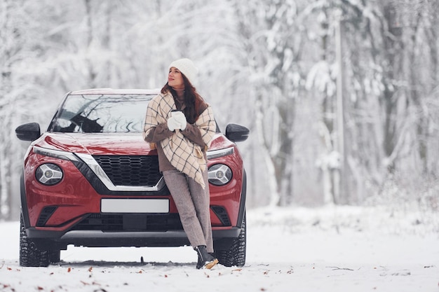 Vor ihrem Auto Schöne junge Frau ist im Winter in der Nähe ihres roten Autos im Freien