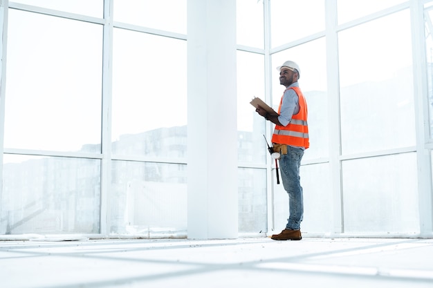 Vorarbeiter bei der Arbeit auf der Baustelle, die seine Notizen in der Zwischenablage überprüft