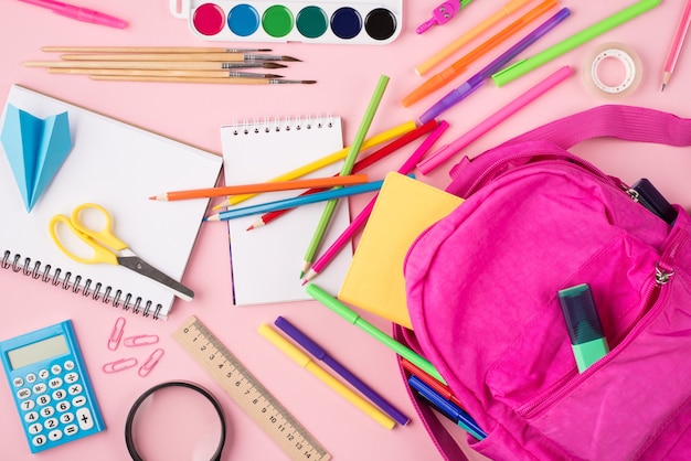 Vorbereitung auf das Schulkonzept. Oben über der Draufsicht Foto von rosa Rucksack und buntem Briefpapier einzeln auf pastellrosa Hintergrund