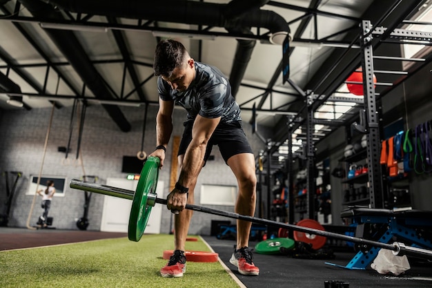 Vorbereitung der Gewichte mit einer Stange zum Trainieren eines starken Muskelbrennens. Ein Mann in Sportbekleidung setzt im Fitnessstudio mit einer Langhantel Gewichte. Cross Fit und Boot Camp Training