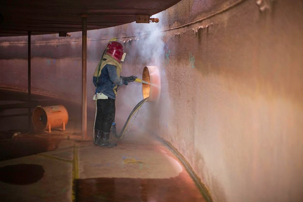 Vorbereitung der Oberflächenkorrosionsplatte durch männliche Arbeiter durch Sandstrahlen des Öls im Inneren des Tanks