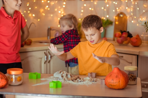 Vorbereitung für den Feiertag Halloween. Drei fröhliche Kinder machen in der Küche Kekse