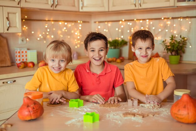 Vorbereitung für den Feiertag Halloween. Drei fröhliche Kinder machen in der Küche Kekse