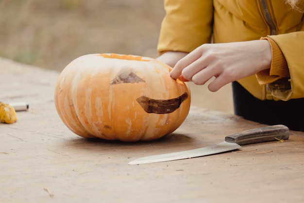 Vorbereitung für Halloween: Mädchen, das Kürbis schneidet. Nahaufnahme. Feiertagsdekorationskonzept. Frau bereitet Jack-O-Laterne vor. Dekorationsparty. Kleiner Helfer.