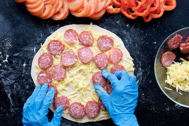 Vorbereitung Pizza im Restaurant in Silikonhandschuhen auf schwarzem Tisch