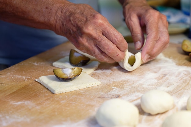 Vorbereitung von hausgemachten Fruchtknödeln mit Pflaumen tschechische Spezialität von süßem gutem Essen Teig auf Küchenholztisch mit den Händen