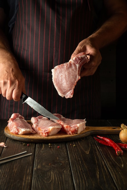 Vorbereitung zum Braten von Fleischrippen Koch mit einem Steak in der Hand in der Restaurantküche, bevor er ein köstliches Mittagessen zubereitet