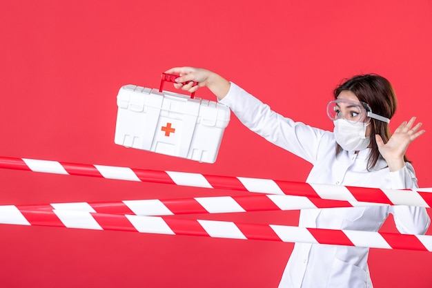 Foto vorderansicht ärztin mit erste-hilfe-set auf rotem hintergrund gesundheitslinie covid-virus medizinische kriminalität krankenhaus gefahr versiegelte heilung