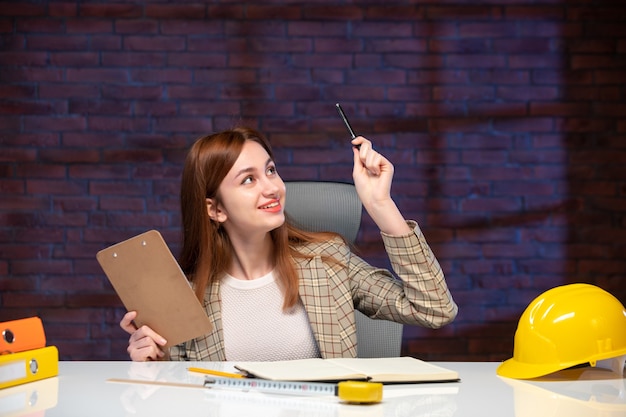 Vorderansicht Arbeiterin auf der Baustelle hinter Tisch sitzend mit Dokumenten Job Unternehmensplan Manager Ingenieur Projekt Agenda Business