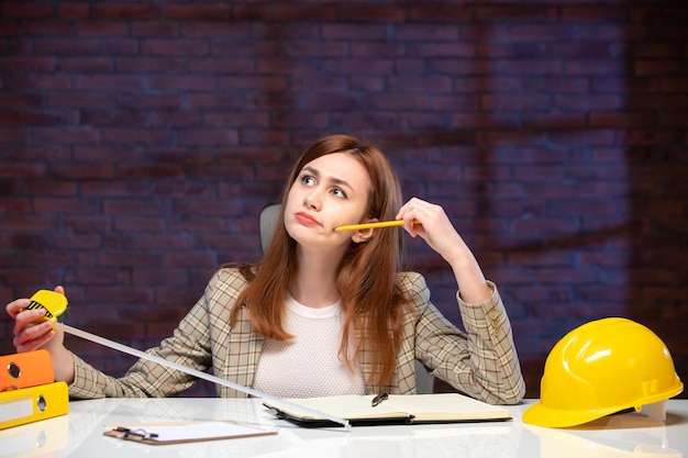 Vorderansicht denkende arbeiterin auf der baustelle, die maßband hält und notizen schreibt agenda engineer corporate project business job