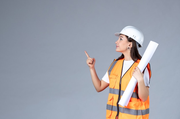 Vorderansicht der Baumeisterin in Uniform mit Poster in den Händen auf weißer Wand