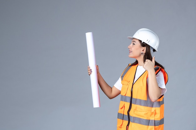 Vorderansicht der Baumeisterin mit Poster in den Händen an grauer Wand