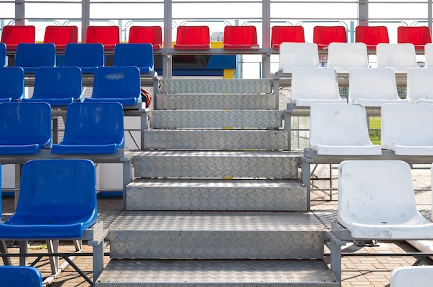Vorderansicht der blauen und roten Plaktiksitze auf der Haupttribüne des Sportstadions mit Metallschritten