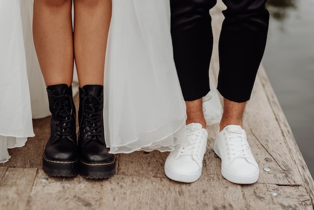 Vorderansicht der Füße des Hochzeitspaares, die auf der Holzbrücke stehen. Vorderansicht der schwarzen und weißen Schuhe.