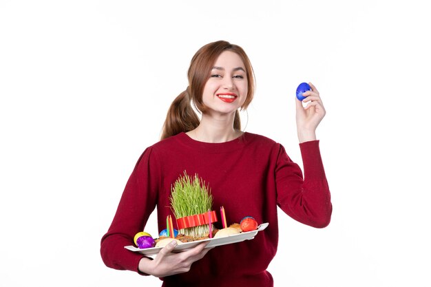 Vorderansicht der jungen Frau, die Honca mit Semeni und Novruz-Bonbons mit blauem Ei auf weißem Hintergrund hält Frühlingskonzept Ethnizität Feriendarsteller ethnische Farben