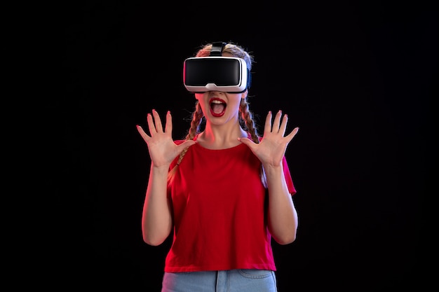 Vorderansicht der jungen Frau, die virtuelle Realität auf dunkler Wand spielt
