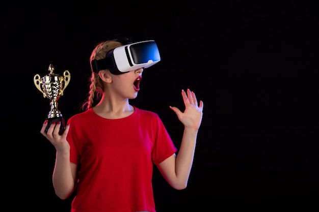 Vorderansicht der jungen Frau, die vr spielt und den Pokal auf dunklem Spiel-Tech-Visual gewinnt