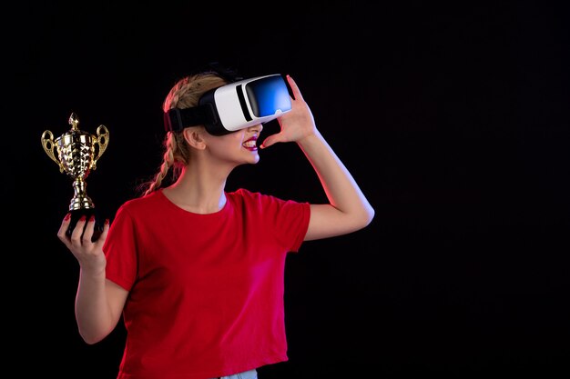 Vorderansicht der jungen Frau, die vr spielt und den Pokal auf dunklem Spiel visueller Technologie gewinnt