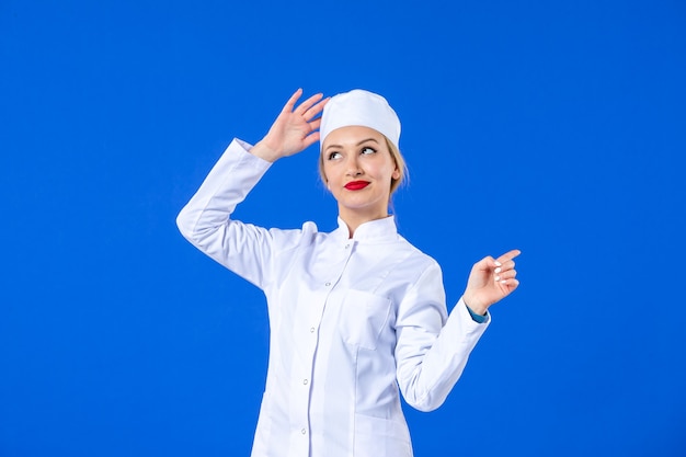 Vorderansicht der jungen koketten Krankenschwester im weißen medizinischen Anzug auf blauem Hintergrund Pandemie-Krankheit Covid-Medizin-Krankheit-Drogen-Virus-Gesundheit