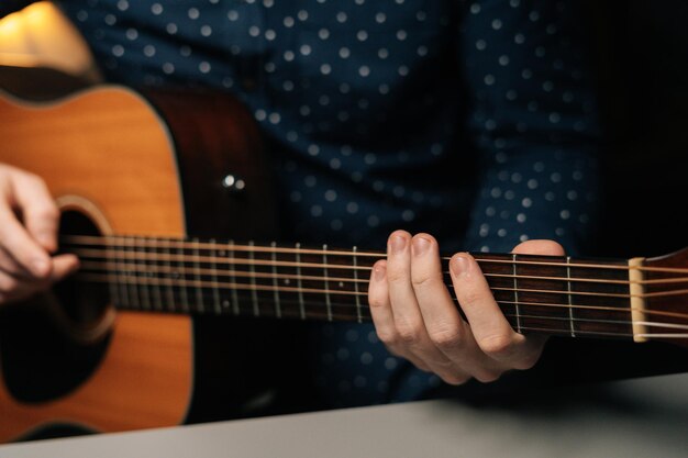 Vorderansicht der Nahaufnahme des nicht erkennbaren Gitarristen, der Akustikgitarre spielt, sitzend am Schreibtisch im dunklen Wohnzimmer, selektiver Fokus Kreativer Musiker, der Freizeitaktivitäten in der Wohnung genießt