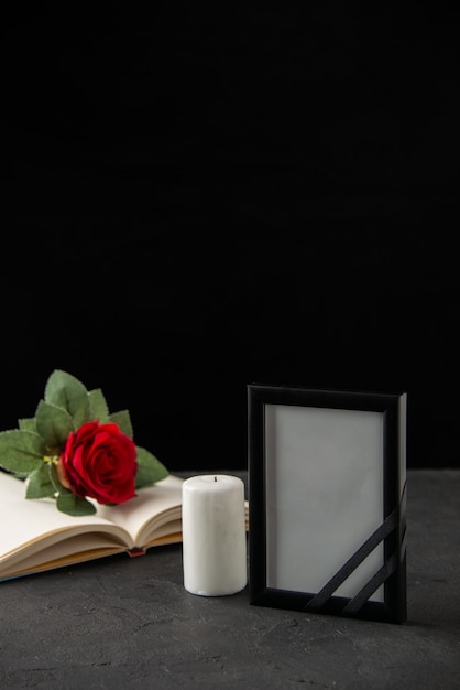Vorderansicht der roten Rose mit Buch und Bilderrahmen auf Schwarz
