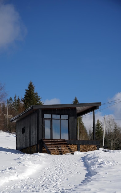 Vorderansicht der schwarzen modernen Holzhütte auf schneebedeckten Bergen