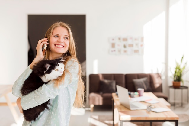 Foto vorderansicht der smiley-frau, die von zu hause aus arbeitet, während katze hält