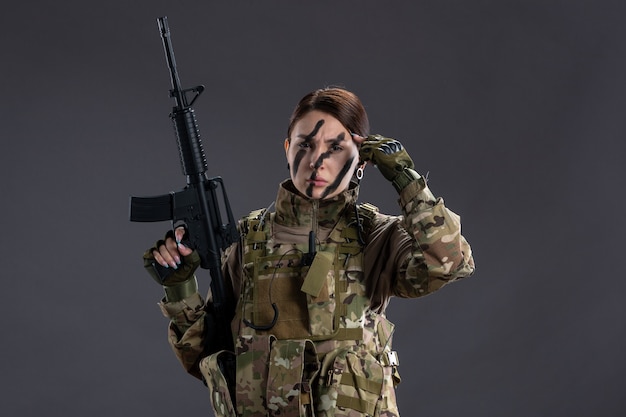 Vorderansicht der Soldatin in Tarnung mit Maschinengewehr an dunkler Wand