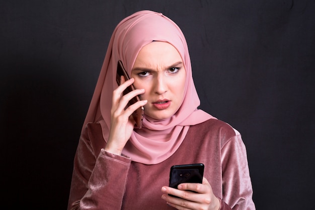 Vorderansicht der verärgerten Frau sprechend auf Mobiltelefon gegen schwarzen Hintergrund