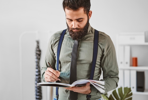 Foto vorderansicht des bärtigen männlichen modedesigners im atelier mit notizbuch