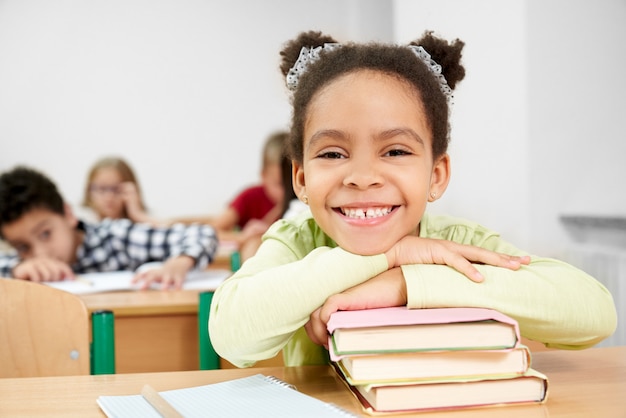 Vorderansicht des glücklichen afrikanischen Mädchens, das auf Büchern liegt und lacht