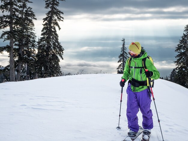 Vorderansicht des jungen aktiven Sportmannes auf Skiern oder Splitboard-Skitouren