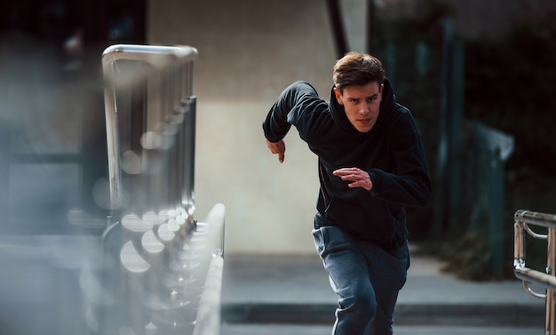 Foto vorderansicht des jungen läufers in schwarzer kleidung, der in der stadt ist.