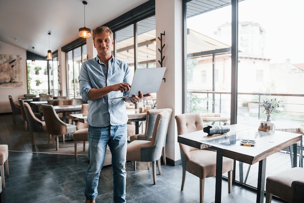 Vorderansicht des Kerls, der tagsüber mit seinem Laptop in einem modernen Café ist.