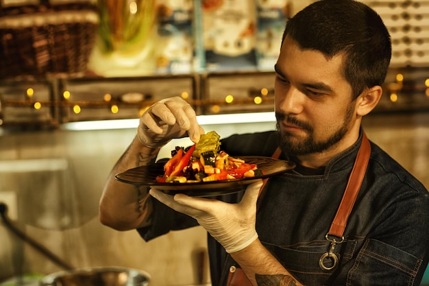 Vorderansicht des Küchenchefs, der ein Gericht mit köstlichem Gemüsesalat hält und es betrachtet. Küchenchef überprüft die Zutaten des Salatkonzepts für kulinarische Speisen und Gastronomie