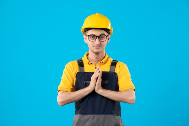 Vorderansicht des männlichen Baumeisters in der gelben Uniform und im Helm auf blauer Oberfläche