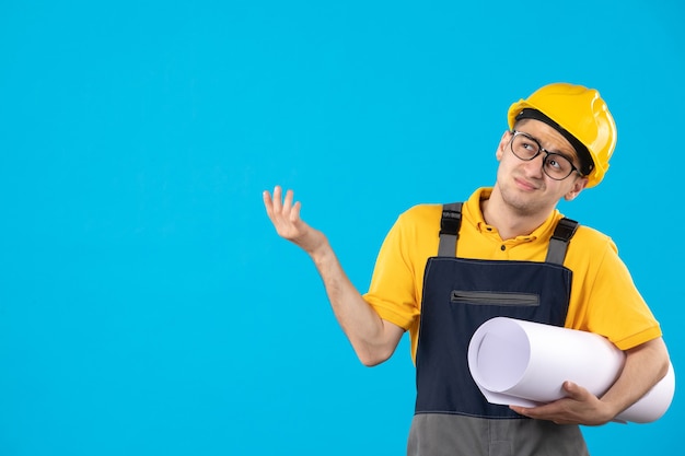 Vorderansicht des männlichen Baumeisters in Uniform mit Papierplan auf blauer Wand