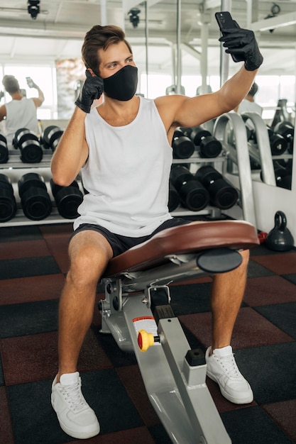 Vorderansicht des Mannes mit der medizinischen Maske, die ein Selfie an der Turnhalle nimmt