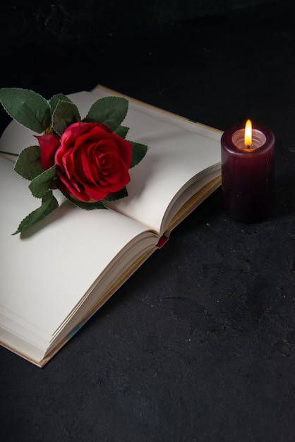 Vorderansicht des offenen Buches mit Kerze und roter Blume auf Schwarz