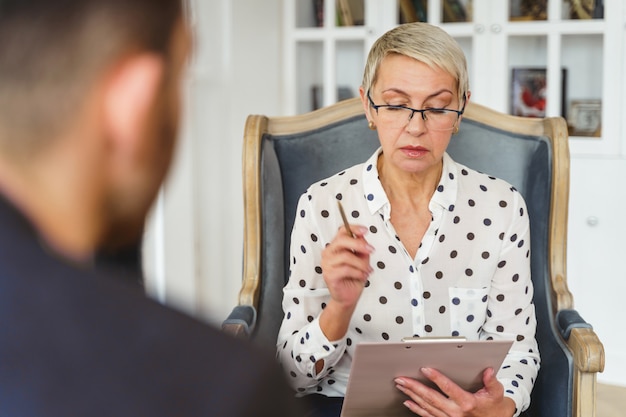 Vorderansicht einer älteren Psychotherapeutin, die während der Therapiesitzung auf ihre Notizen starrt