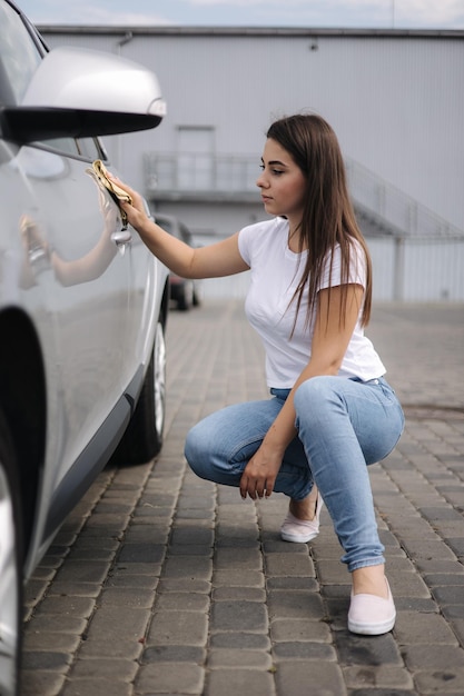 Vorderansicht einer attraktiven, fröhlichen, fröhlichen Fahrerin, die ihr Auto mit speziellem Lappen in Selbstbedienung wäscht