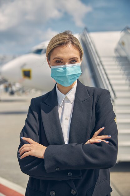 Vorderansicht einer eleganten blonden kaukasischen Dame mit verschränkten Armen, die am Flughafen steht