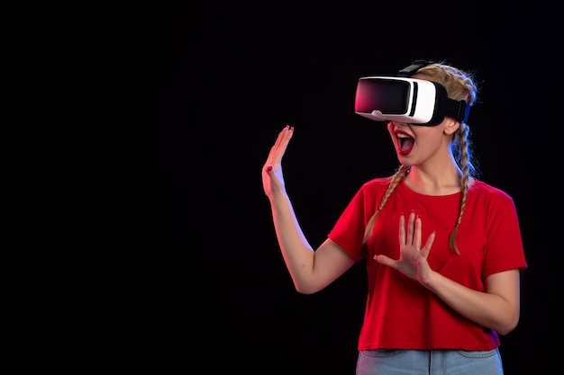 Vorderansicht einer jungen Frau, die vr an einer dunklen Wand spielt