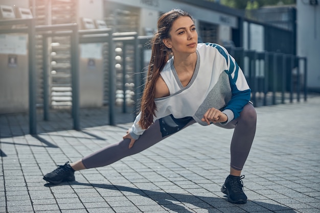 Vorderansicht einer jungen sportlichen Frau mit langen dunklen Haaren, die einen seitlichen Ausfallschritt macht