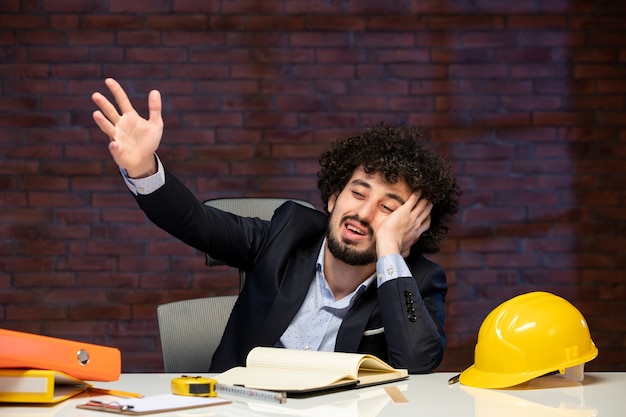 Foto vorderansicht eines gelangweilten männlichen ingenieurs, der hinter dem arbeitsplatz im anzug des bauunternehmers sitzt