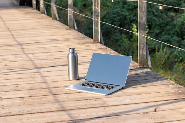 Vorderansicht eines isolierten Laptops und einer Flasche Wasser eines digitalen Nomaden auf einem Holzboden mit Kopierraum